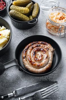Fried Bavarian German Nürnberger sausages with sauerkraut, mashed potatoes in cast iron frying pan, on gray background