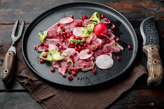 Carpaccio of marbled beef, with Radish and garnet, on plate, on old dark wooden table background