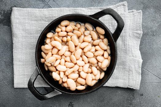 White canned beans, in cast iron frying pan, on gray stone background, top view flat lay