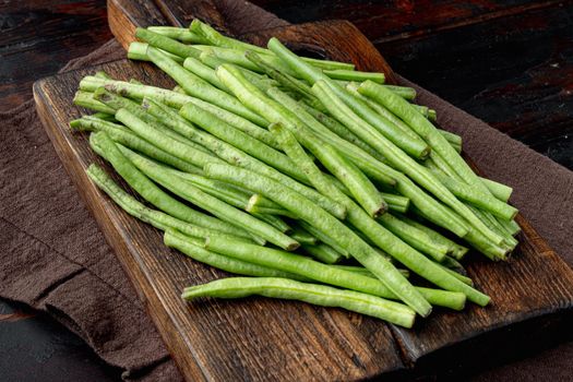Fresh green French beans, on wooden cutting board, on old dark wooden table background