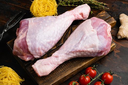 Fresh uncooked turkey legs, on wooden cutting board, on old dark wooden table background
