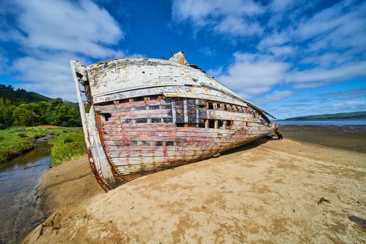 Side hull of red and white shipwreck on sandy beaches with blue sky