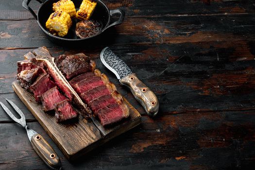 Grilled medium rare t bone or Porterhouse steak, on wooden serving board, on old dark wooden table background, with copy space for text