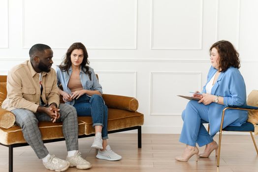 Stressed unhappy millennial Caucasian and African American couple have relationship problems. Diverse couple fighting while visiting professional psychologist for help, breakup prevention concept.