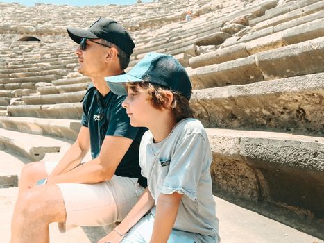 Young father dad and his school boy kid son tourists visiting ancient antique coliseum amphitheater ruins in hot summer day