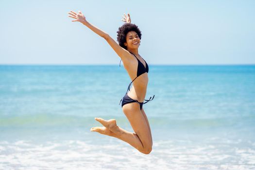 Happy black woman jumping near sea in summer
