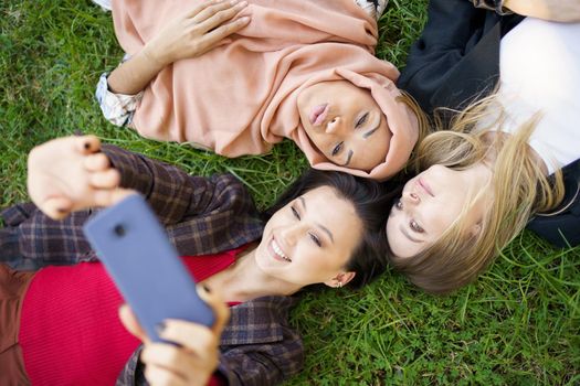 Multiracial girlfriends lying in circle and taking selfie