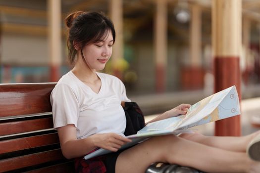 Pretty Young traveler woman looking on maps planning trip at train station. Summer and travel lifestyle concept.