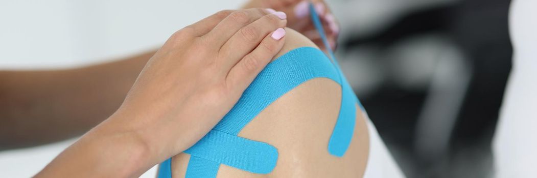Physiotherapist apply kinesiology tape to patient knee in clinic