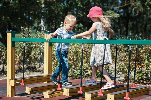 The boy and girl meet each other on a monkey bridge at a city children's playground