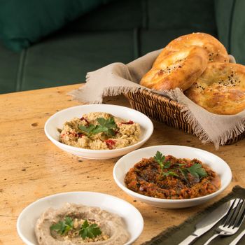 A photo of Mediterranean dishes, baba ganoush, muhammara and hummus with a basket of bread