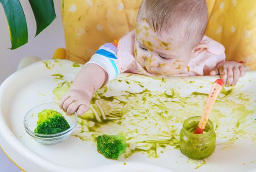 Little baby eats broccoli puree himself. Selective focus.