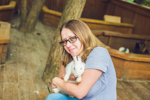 Happy woman with white baby rabbit. Smiling Girl with little Easter bunny. Cute furry hare