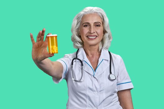Smiling female doctor holding jar with pills and looking at camera on color background.