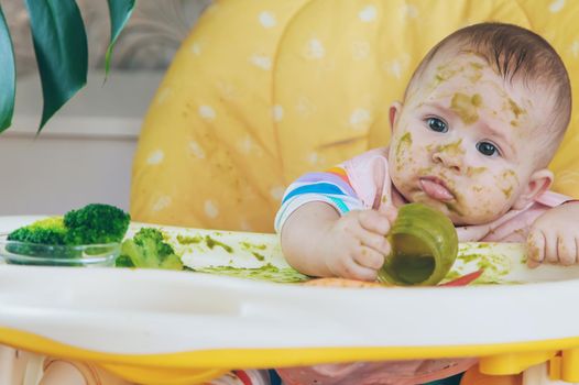 Little baby eats broccoli puree himself. Selective focus.