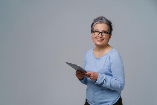 Businesswoman in eye glasses and digital tablet in hands working online smile looking at camera. Pretty woman in 50s in blue blouse isolated on white. Older people and technologies