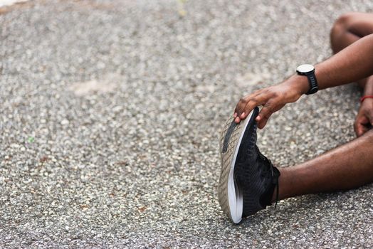sport runner black man wear watch he sitting pull toe feet stretching legs and knee