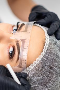 Cosmetologist is measuring with ruler the brows