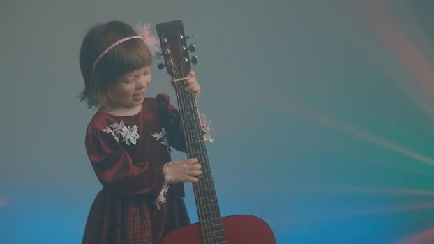 Little girl in a vintage dress plays an acoustic guitar like a double bass