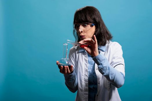 Intrigued and curious chemist holding glass flasks while mixing chemical liquid substances