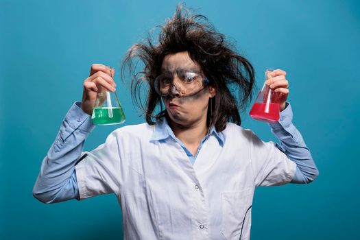 Mad chemist having beakers filled with toxic liquid substances while on blue background.