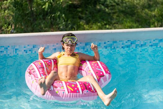 Smiling cute little caucasian girl in outdoor pool in sunny day. The girl is holding on to the side of the pool. Summer, vacation and health care concept