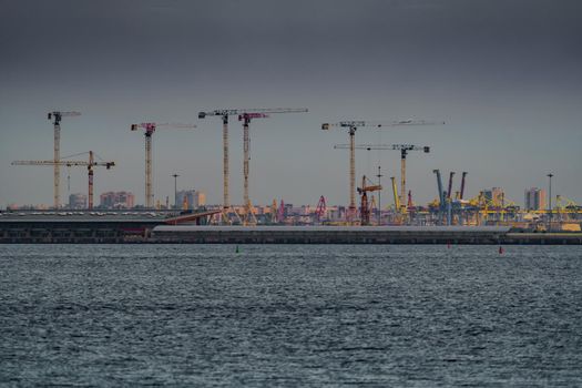Seaport, construction cranes and cranes of the cargo port on the sea horizon in sunset light