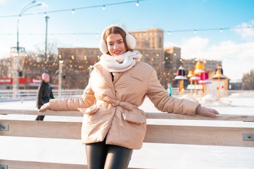 Beautiful lovely young adult woman brunet hair warm winter jackets stands near ice skate rink background Town Square. Christmas mood lifestyle