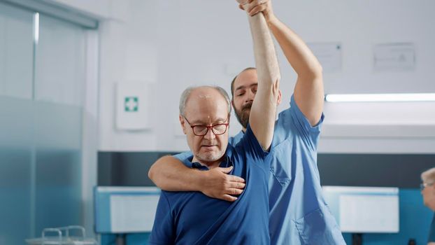 Medical assistant raising arms of elder person to stretch muscles