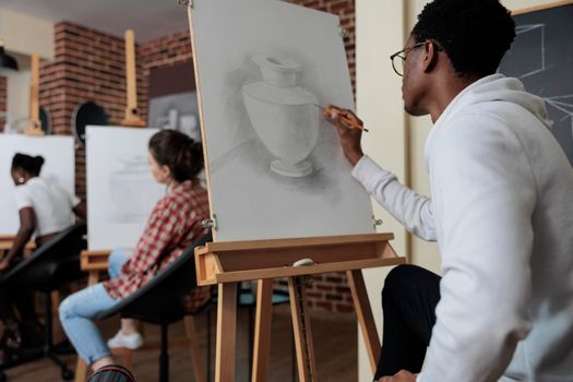 Creative student sitting in front of white canvas drawing vase model