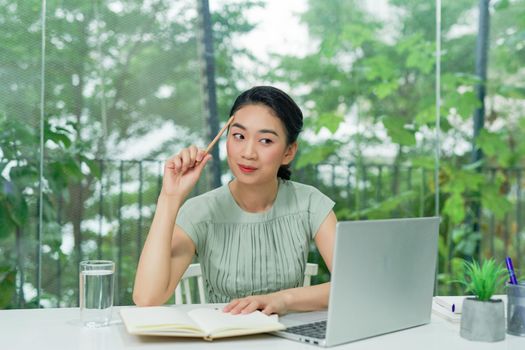 Business Asian young woman working with computer laptop holding pen and thinking to get ideas and requirement