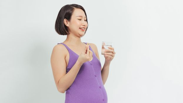  Young pregnant woman holding glass of water and pill.