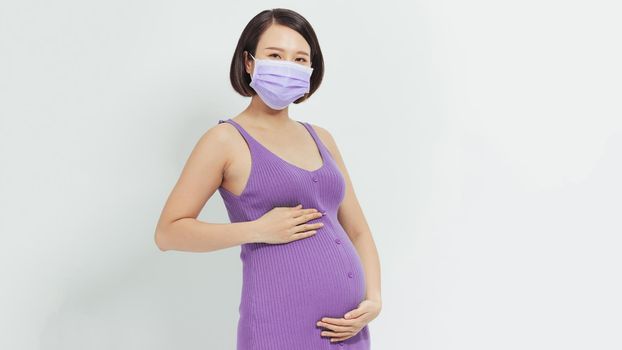 coronavirus pandemic, young pregnant woman in protective medical mask holds on stomach