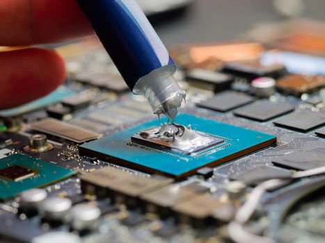 Technician applying thermal paste to a GPU on laptop motherboard.