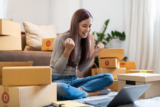 Asian woman working at small business ecommerce with laptop very happy and excited doing winner gesture with arms raised, smiling and screaming for success. celebration concept
