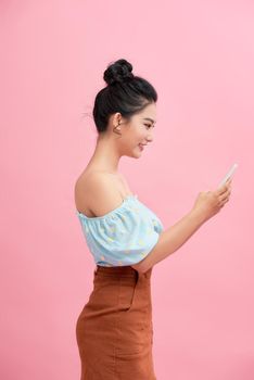 Dreamy asian beauiful young woman holds modern electronic device, isolated over pink background.
