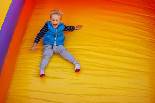 Happy little boy sliding down an a yellow- orange inflatable slide. There is free space for text in the image.