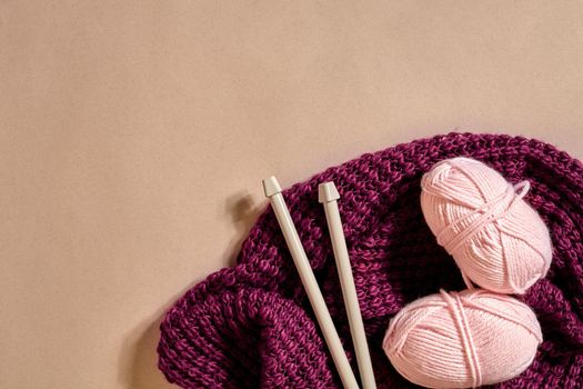 Two pink knitting yarn balls, knitting needles and and purple knitted plaid top view