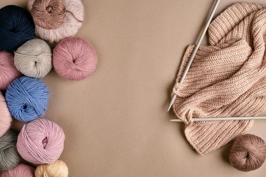 Set of colorful wool yarn and knitting on knitting needles on beige background. Top view