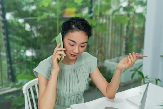 Young office woman holding a pencil while talking on mobile phone at the modern working desk