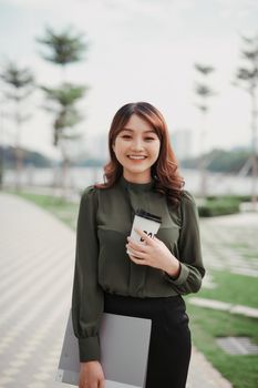 Image of a joyful woman walking with a silver clipboard and takeaway coffee in her hands