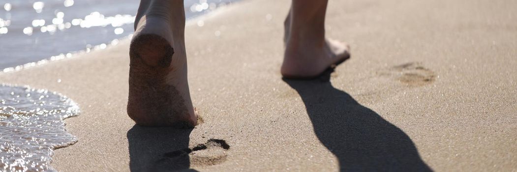 Barefoot female feet walking along sea beach closeup