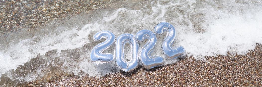 Helium balloons with numbers 2022 lying on sea wave closeup background
