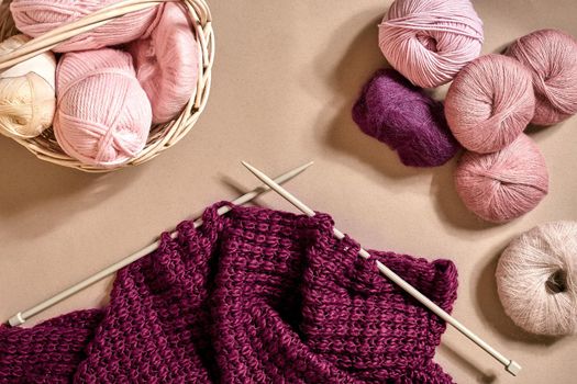 Balls of merino wool yarn, knitting on knitting needles on a beige surface. Top view