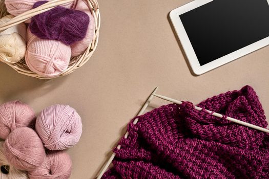 Balls of merino wool yarn, knitting on knitting needles on a beige surface. Top view