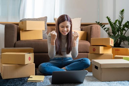 Asian woman working at small business ecommerce with laptop very happy and excited doing winner gesture with arms raised, smiling and screaming for success. celebration concept
