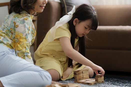 Girl playing wooden jenga constructor with grandmother at home. Leisure activities for children at home.