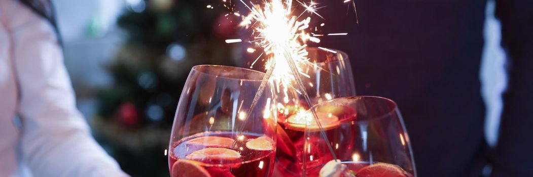 Group of people clinking glasses with alcoholic cocktail and sparklers closeup