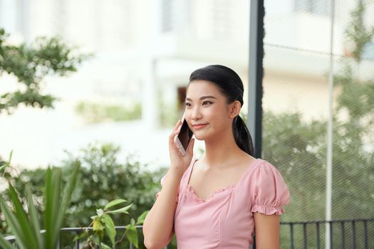 Portrait of cheerful young woman standing on balcony, calling on phone