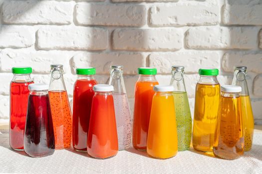 Row of glass bottles of different juices against white brick wall